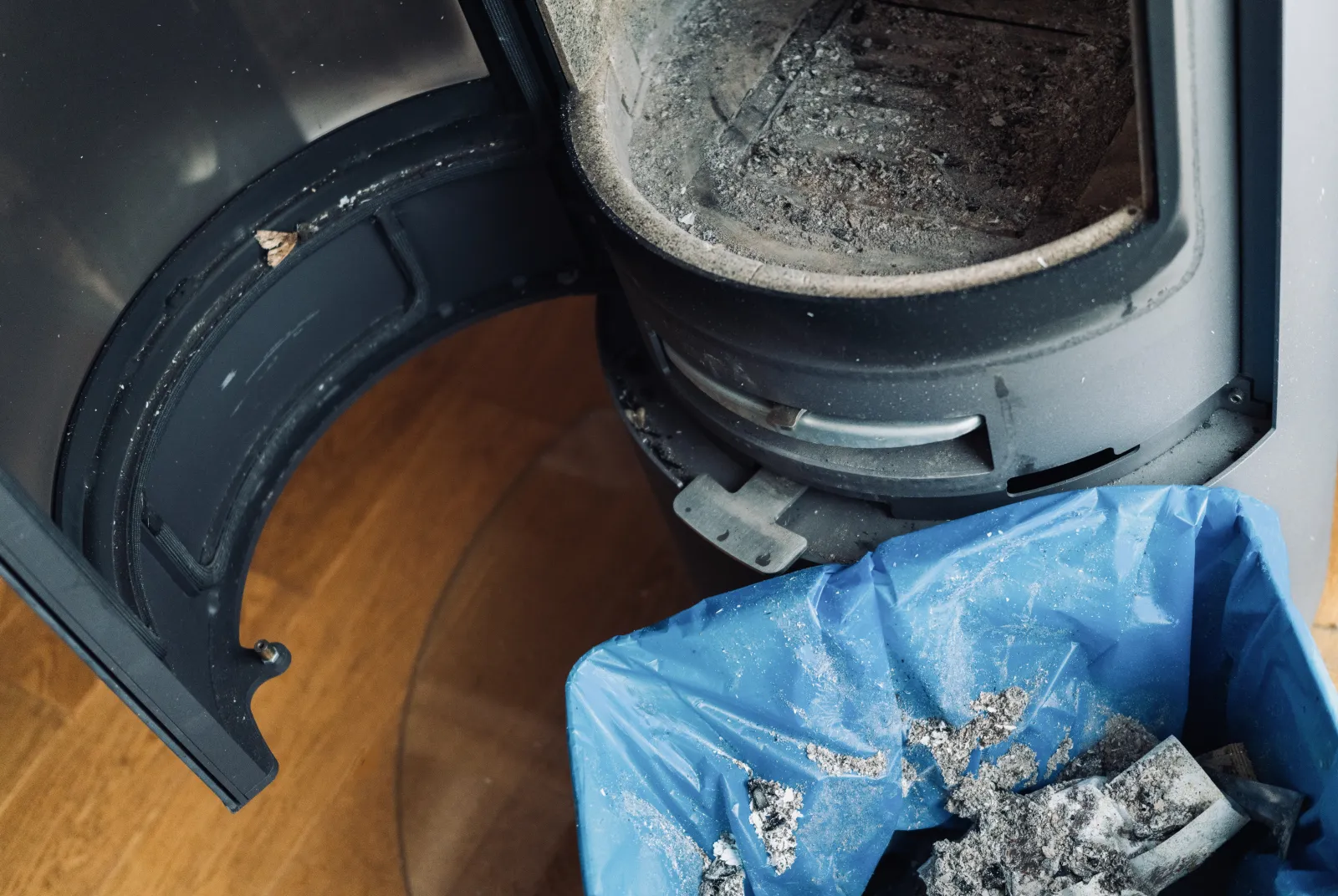 A wood stove cleaned out mid-service — door open, ash bagged for disposal